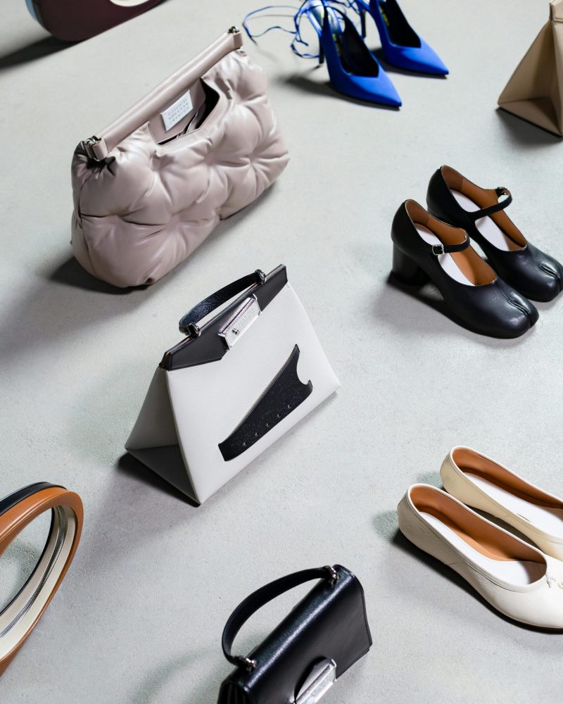 High-angled shot of stylish shoes and bags arranged on a white surface, exuding elegance and luxury.